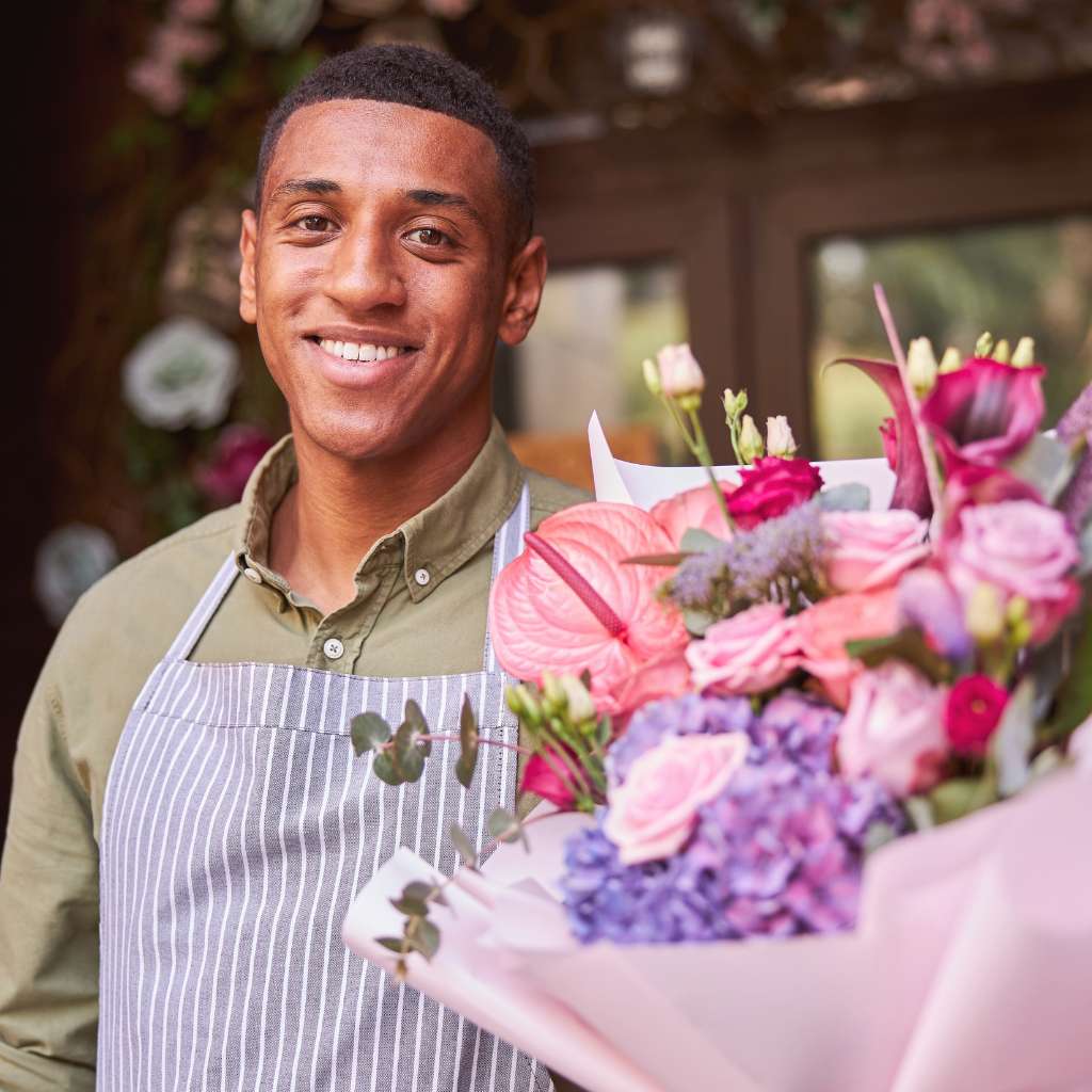Smiling florist holding a bouquet of flowers outside his shop