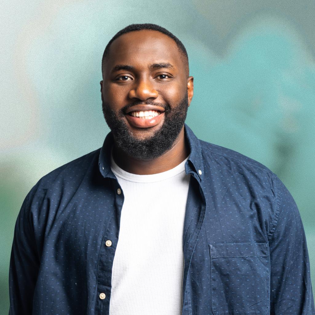 Man wearing a blue shirt over a white t-shirt with a blurred green background
